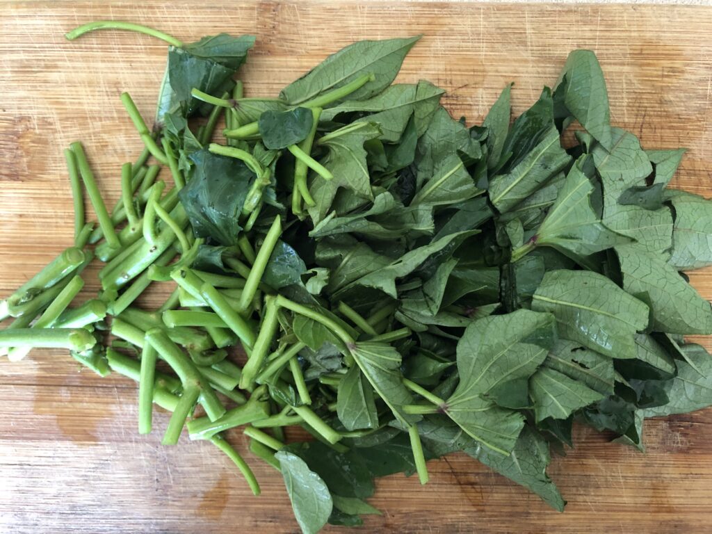 sweetpotato greens that have been roughly chopped on a wooden cutting board