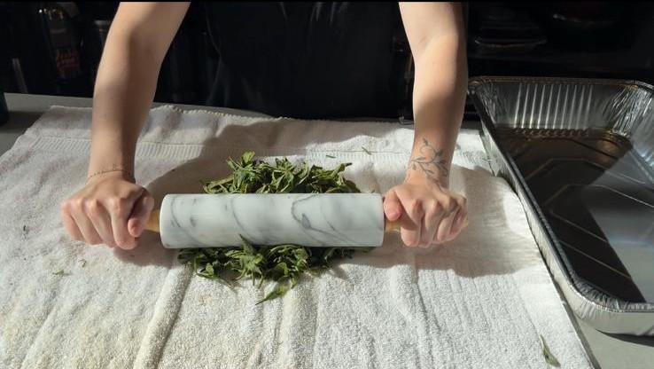 close up of a person rolling leaves with a rolling pin on top of a white towel
