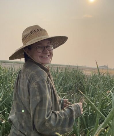 Woman in a wide-brimmed straw hat standing in an onion field.