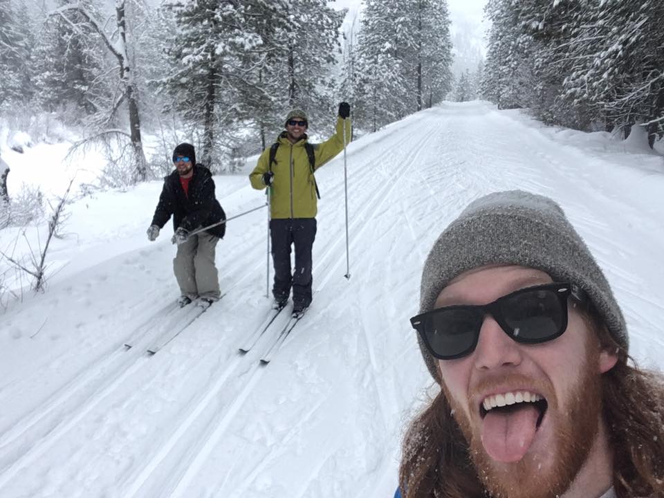 two people cross country skiing posed behind a bearded man taking the picture.