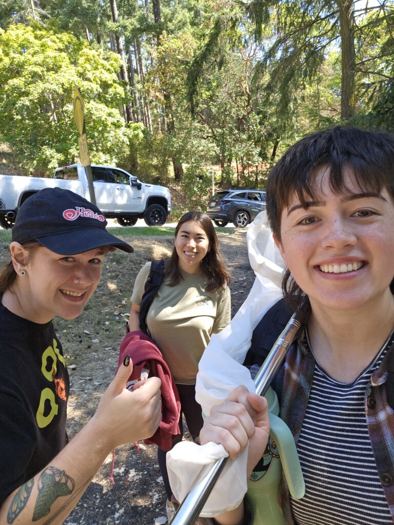 three smiling people are headed out to sample insects; the person on the left is giving a thumbs up, the person in the middle is smiling, and the person on the right is holding an insect net on their shoulder.