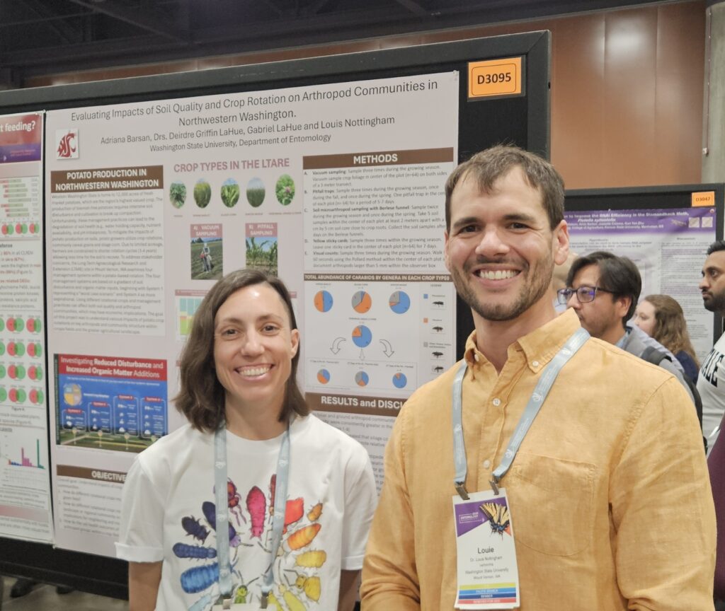 Two people stand in front of an award-winning poster; the person on the left is wearing a colorful bug shirt.