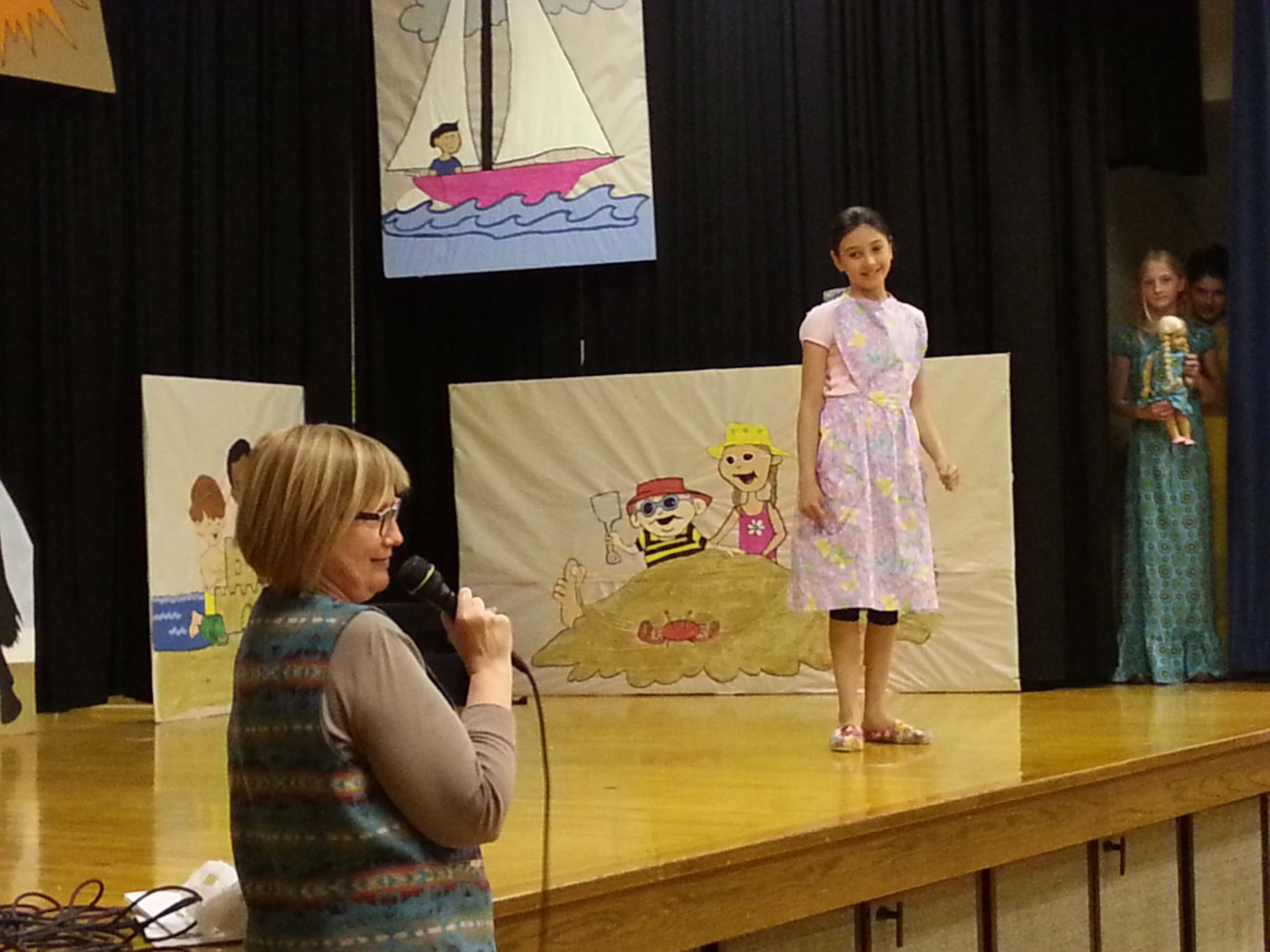 Youth modeling a light purple dress on stage while an adult describes the outfit