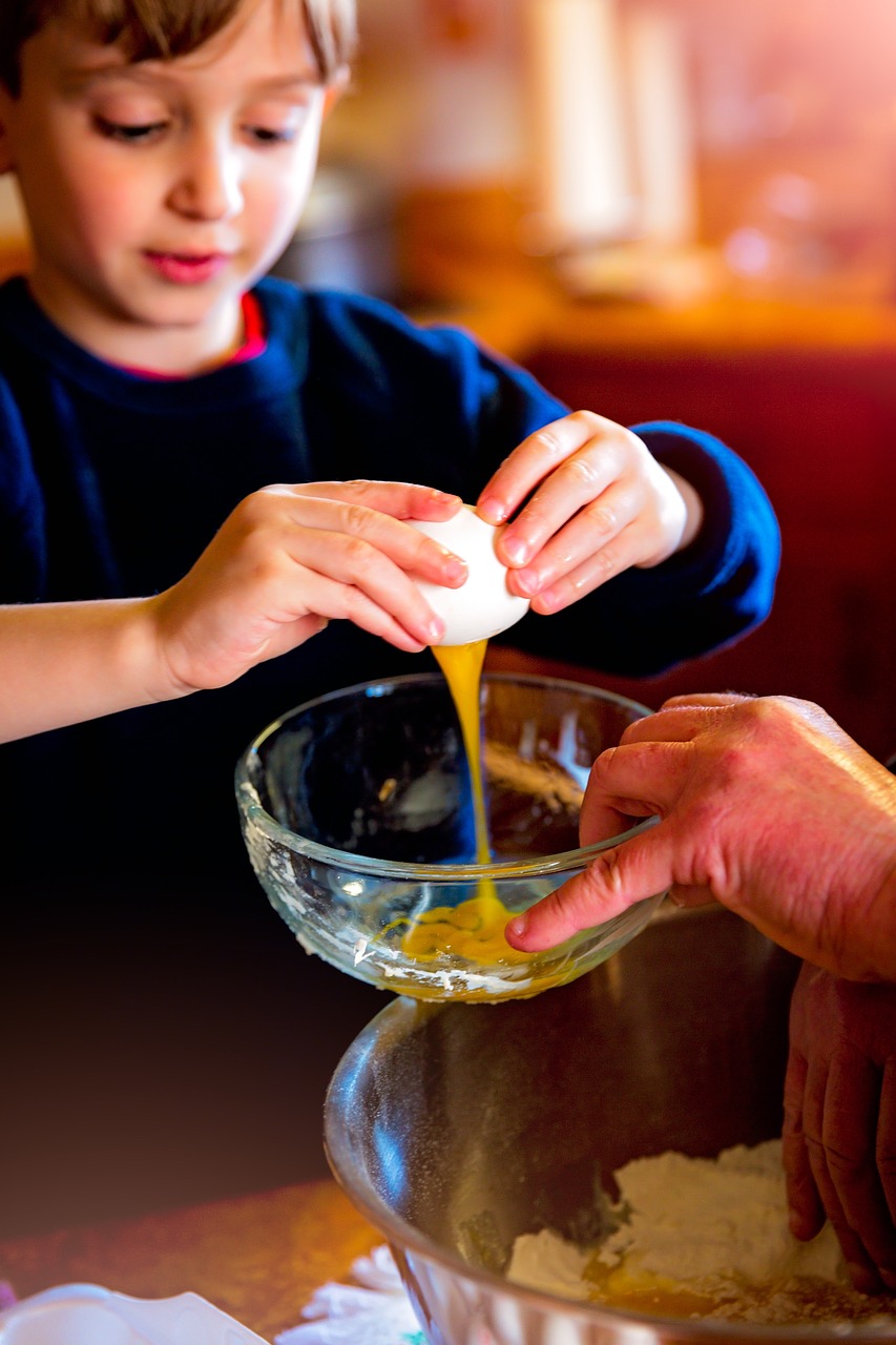 A youth cracking an egg into a glass bowl held up by an adult standing out-of-frame
