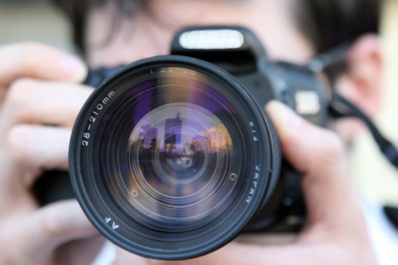 Close up of a camera lens with blurred person holding the camera in the background.