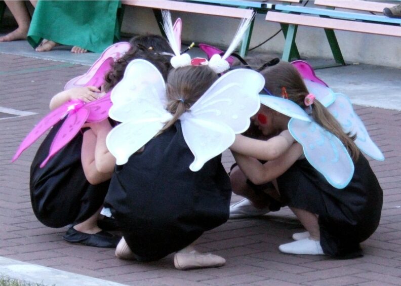 A small group of children wearing butterfly wings crouch in a circle facing inward.