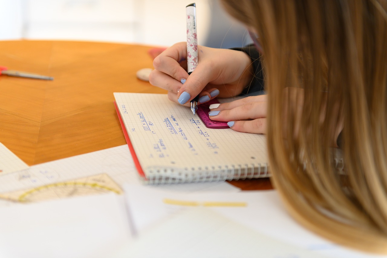 Close cropped image of a girl writing in a notebook; her hair is visible, her face is not.