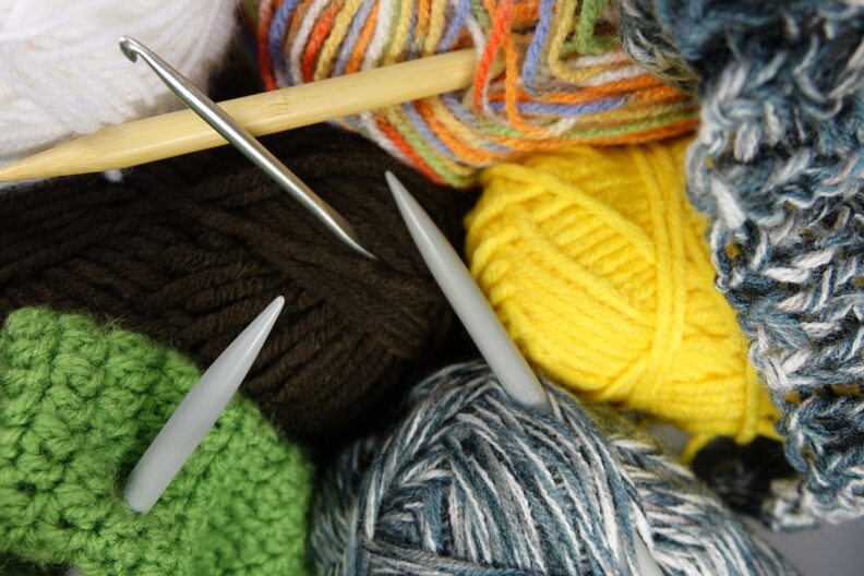 A crochet hook and knitting needles stuck through balls of yarn and unfinished projects.