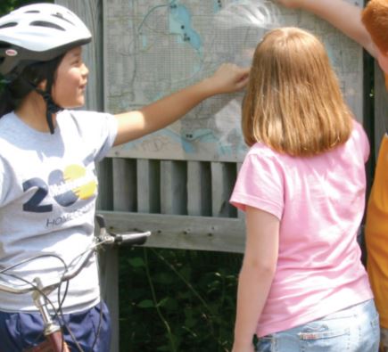 Two young people, one with a bicycle and wearing a helmet, look at a map of a city.