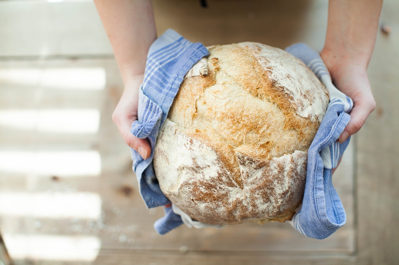 A fresh baked loaf of bread wrapped in a towel, held by two hands with the rest of the person off-camera
