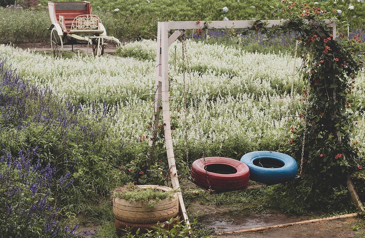 Wildflower garden with a swing in the foreground with tires laying flat as its seat and another tire as a planter beside it. In the background, an antique carriage as a seating spot