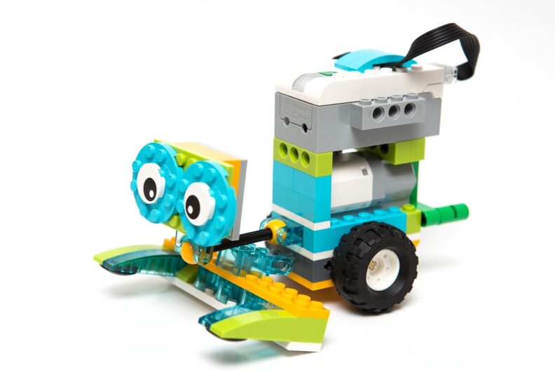 A LEGO WeDo robot with a yellow and green forklift style front, eyes on a blue forward-facing platform, and a blue "body" with a gray sensor on top and wheels at the bottom