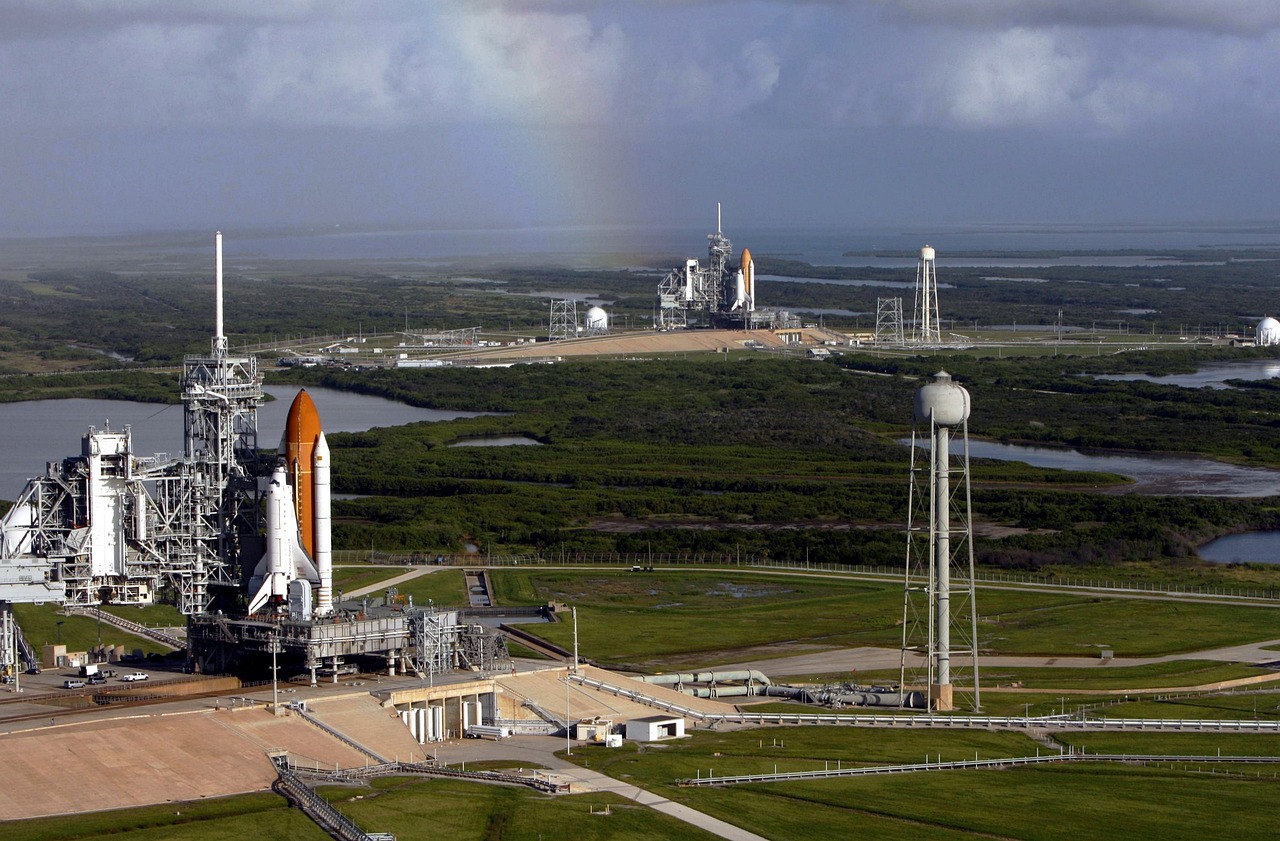 Two space shuttles in launch configuration at Kennedy Space Center in Florida - the sky has a few clouds and there is a rainbow above them