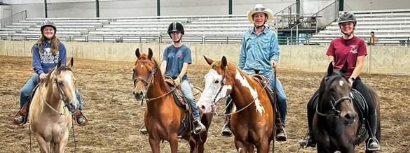 Four teen youth on horseback in a show arena with empty stands
