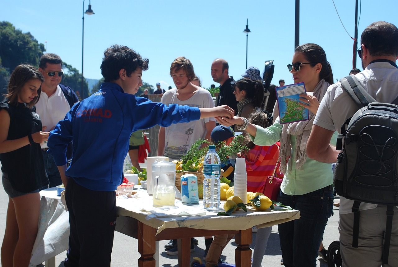 A teenager sells fresh made lemonade to a crowd, handing change to an adult in front of them