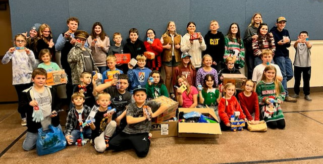 A large group of youth hold up personal care items, food, and other necessities donated to a project to help homeless kids