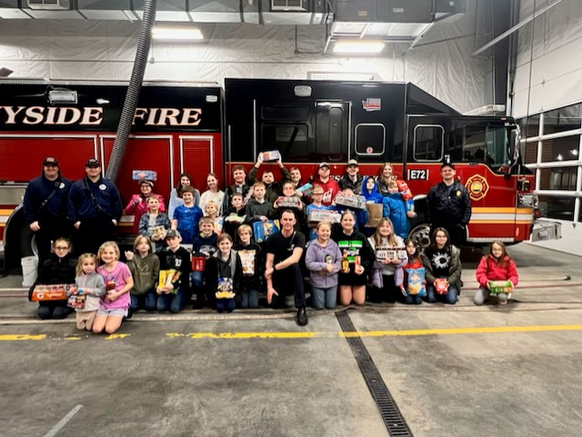 A group of youth and firefighters pose together in front of a fire truck