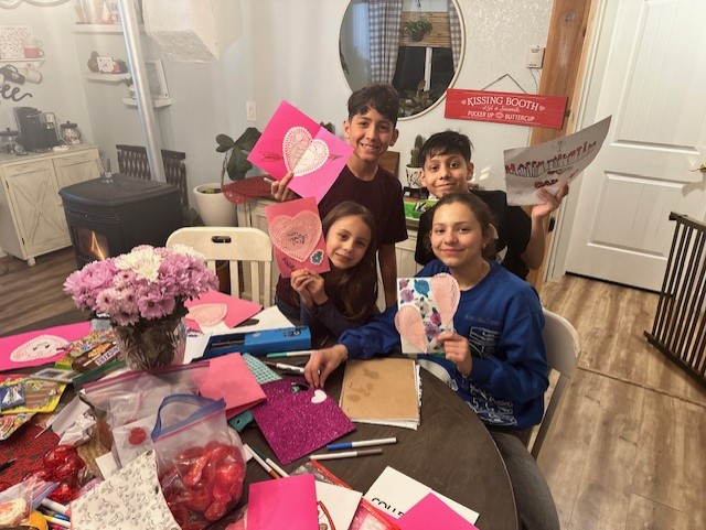Youth holding hand-made Valentine's Day cards while sitting at a table with the supplies to make them