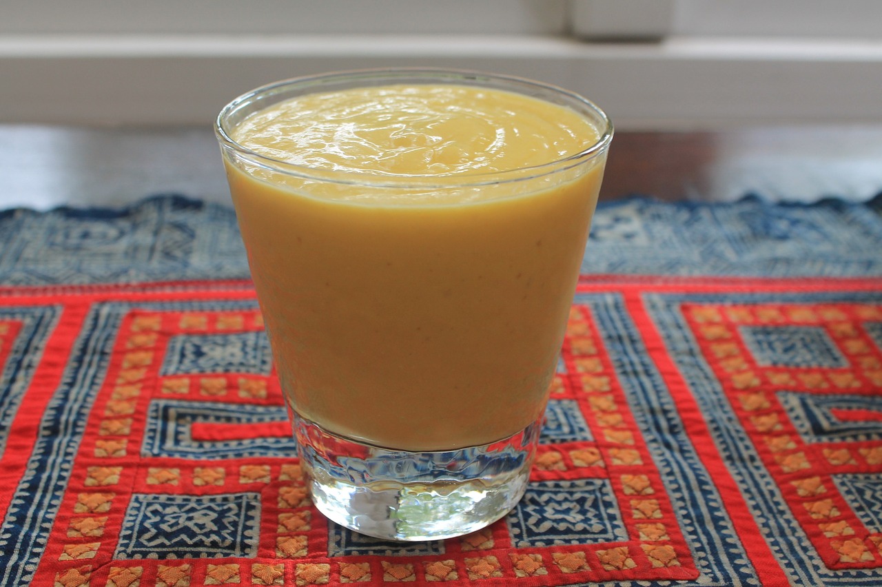 A wide-rimmed glass containing mango smoothie on a red and blue geometric patterned tablecloth.