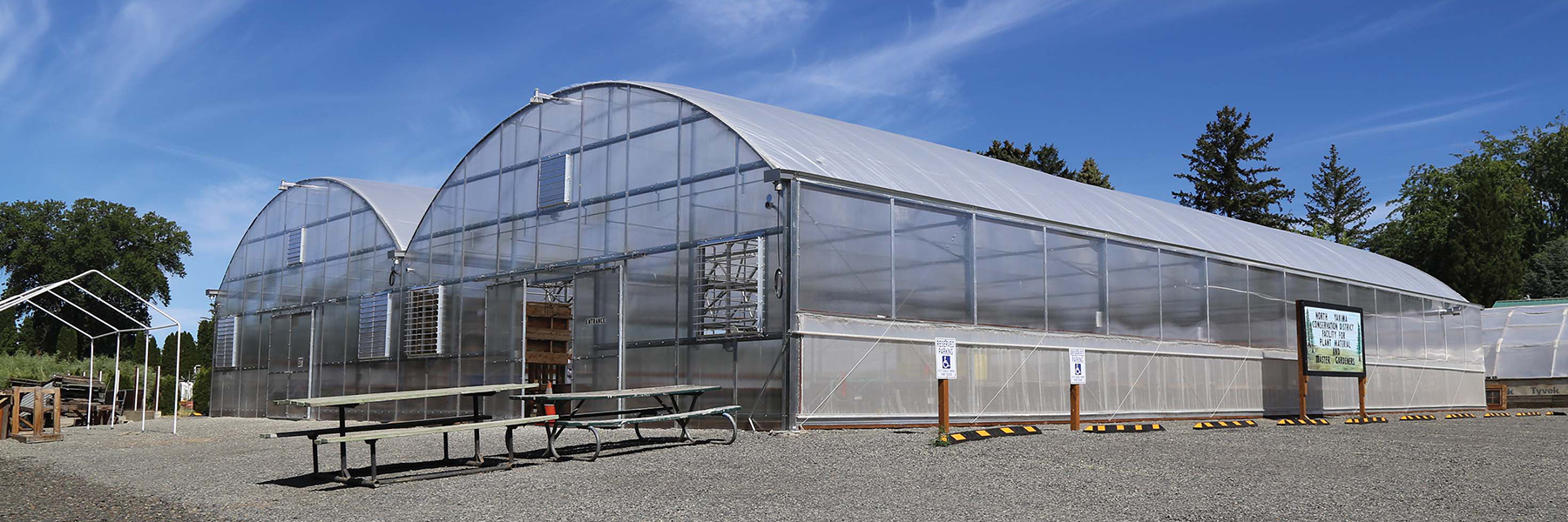 Two large curved-top greenhouses against a blue sky with light clouds.