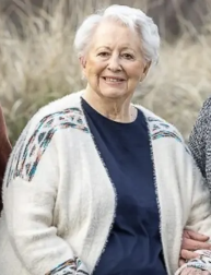 Light skinned woman with short white hair smiling while wearing a navy blue shirt and cream colored cardigan