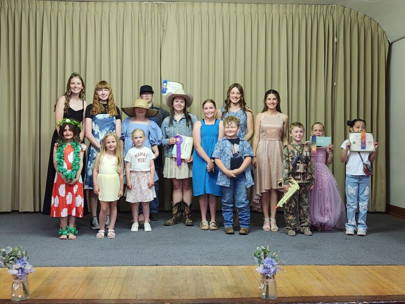 Youth from ages 5 to 19 standing on a stage smiling while holding ribbons and certificates.