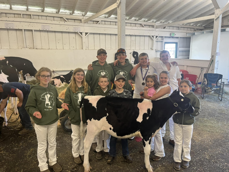 Group of youth members smiling for the photo while standing surrounding a baby cow.