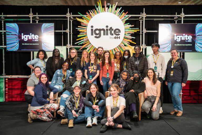 Large group of teens posing for picture in front of a sign that state "ignite by 4-H" to advertise the ignite teen conference