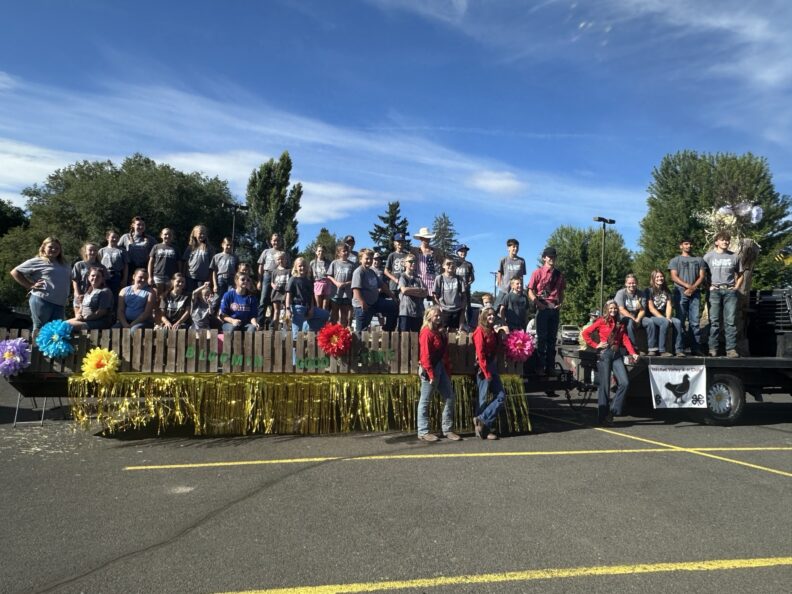 Large group of children wearing grey shirts that say "Naches Valley 4-H Club while standing on a parade float smiling for the picture