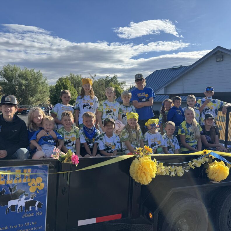 Youth wearing blue and white shirts that state "Selah 4-H" while sitting smiling on their float about to go in the parade at West Valley Fair