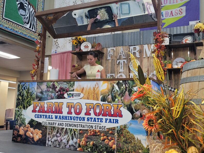 Girl cooking on the Farm to Fork Stage with a mirror above her reflecting her griddle as she flips the ingredients using a pink spatula.