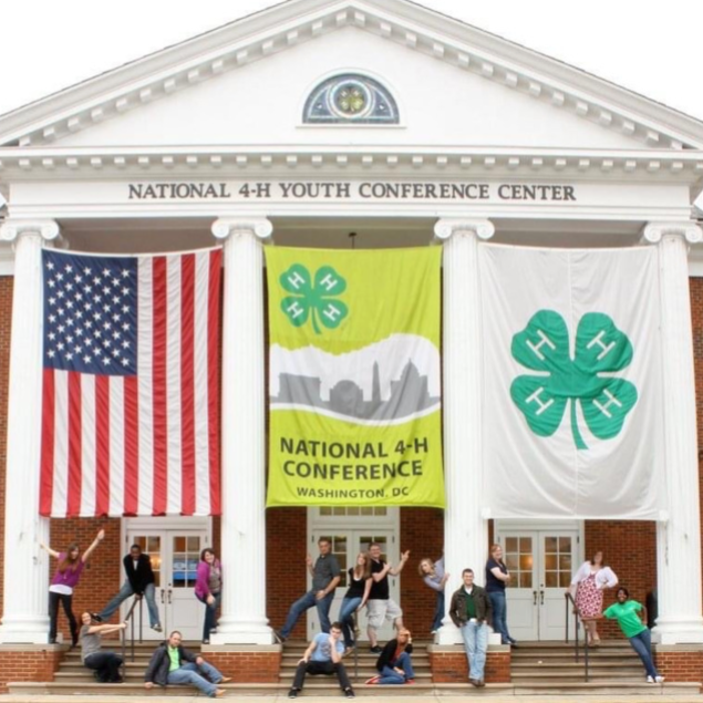 A group of youth in front of the National 4-H Youth Conference Center and large banners for the National 4-H Conference.