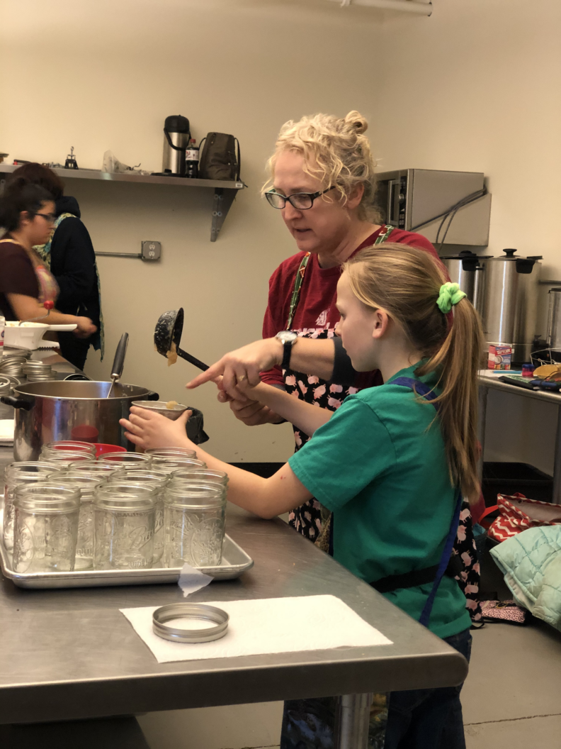 An adult volunteer helps a youth prepare applesauce for canning