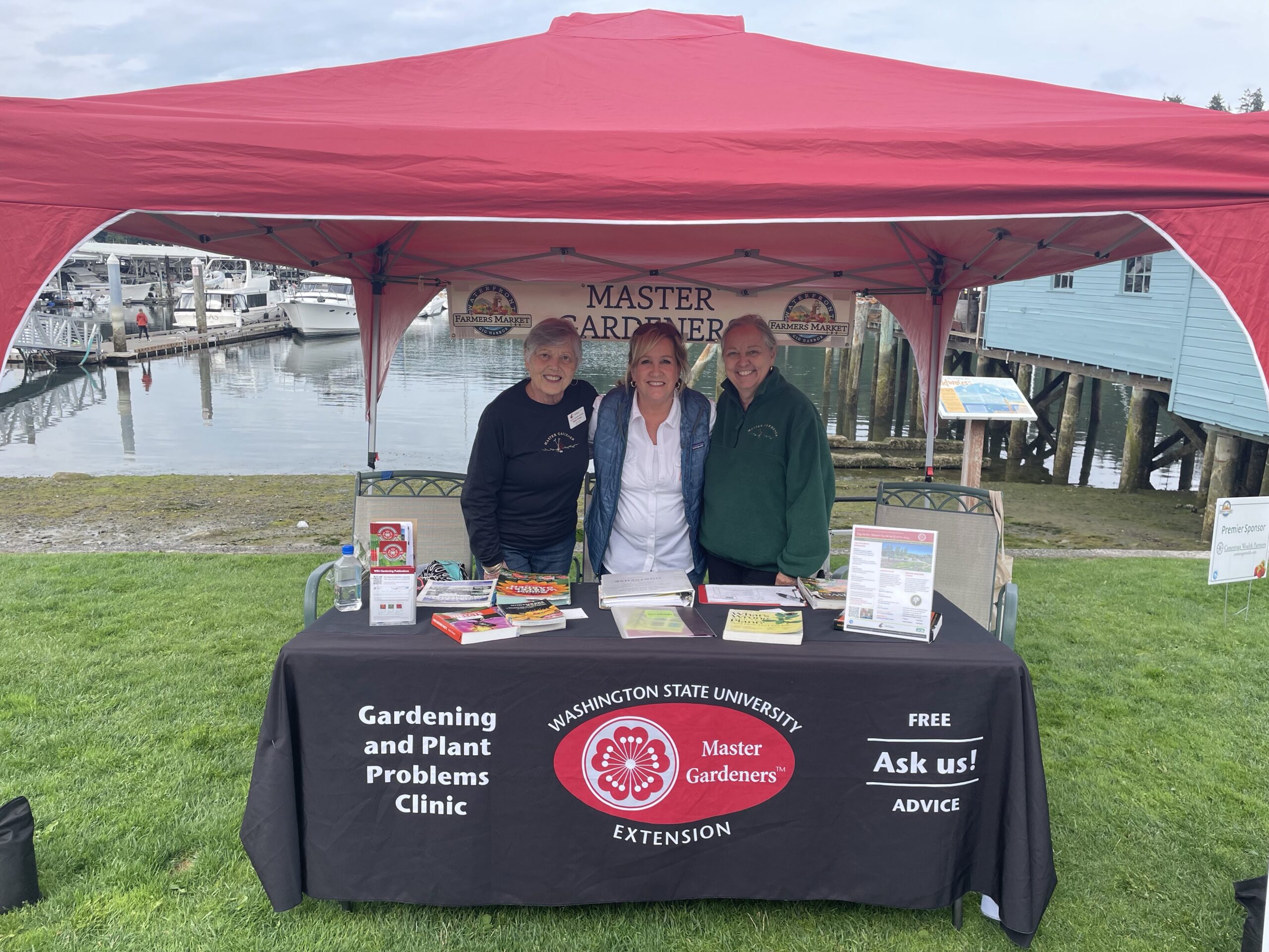 Three women under a canopy at a farmers market booth.
