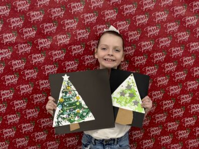 Cloverbud Member holding picture she designed by painting a Christmas Tree with a fork.