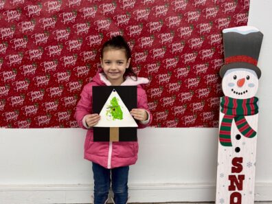 Cloverbud Member holding picture she designed by painting a Christmas Tree with a fork.