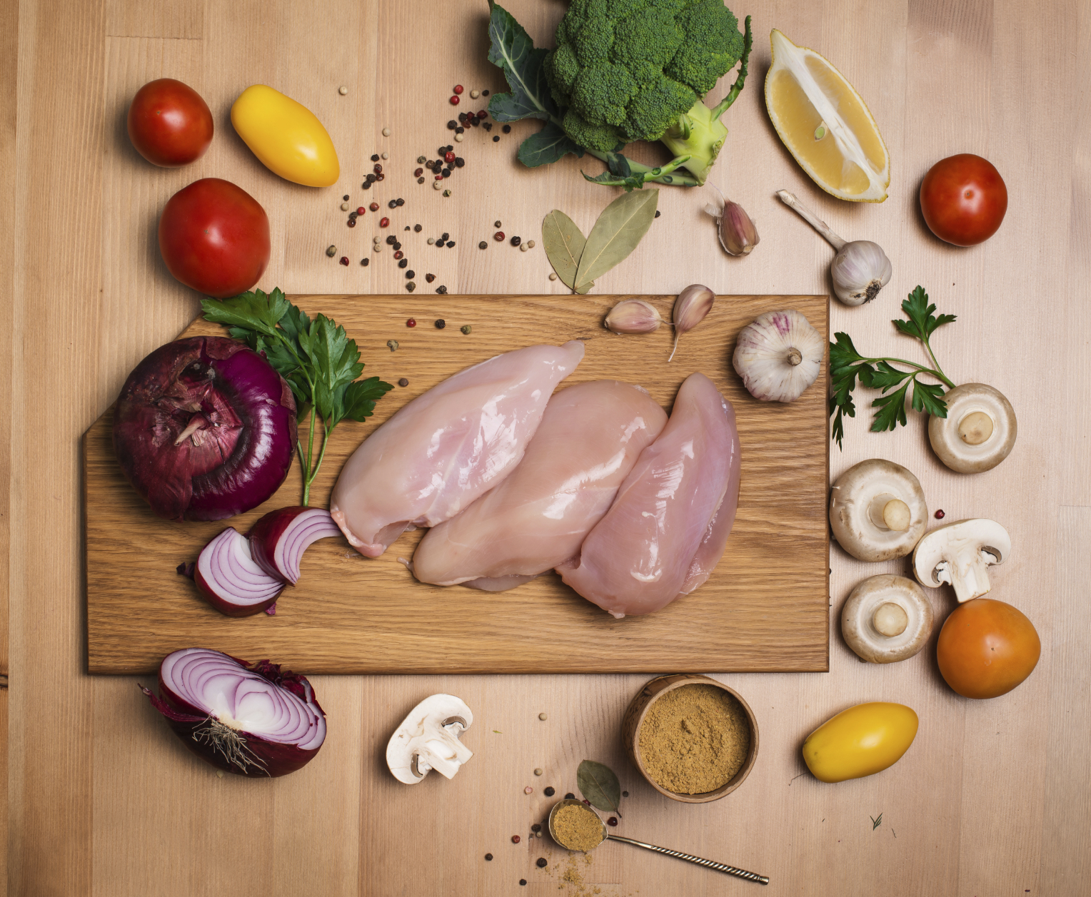 Raw Chicken on a cutting board surrounded by other vegetables and spices.