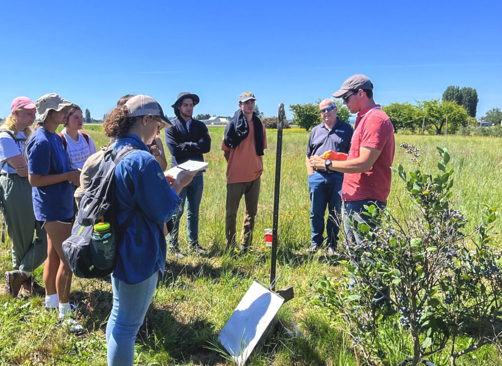 Man giving a presentation next to a blueberry bush.