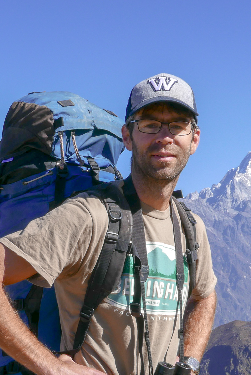 Man wearing a backpack; mountain in the background.