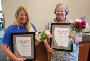 Two women holding flowers and framed certificates.