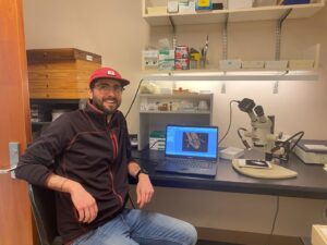 Man sitting in microscopy lab, turned to the camera.