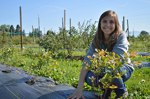 Lisa Wasko DeVetter crouches near young blueberry bushes.