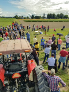 Tractor in foreground as large group listens to a field presentation.