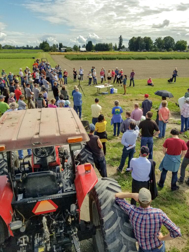 Tractor in foreground as large group listens to a field presentation.