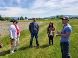 Three people listen to a young man talking in a field.