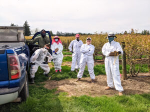 Six people in coveralls standing next to berry field.
