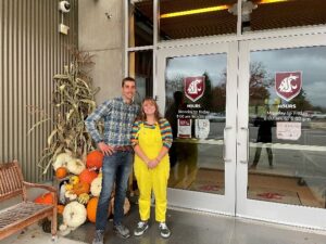 Two people stand in front of glass doors.