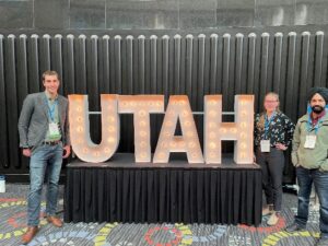 Three people standing next to lighted "UTAH" sign.