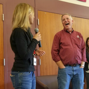 Woman holding microphone talks to man in crimson shirt during a presentation.