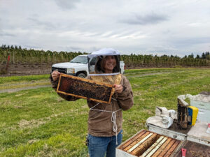 Woman in hood holding a bee hive frame.